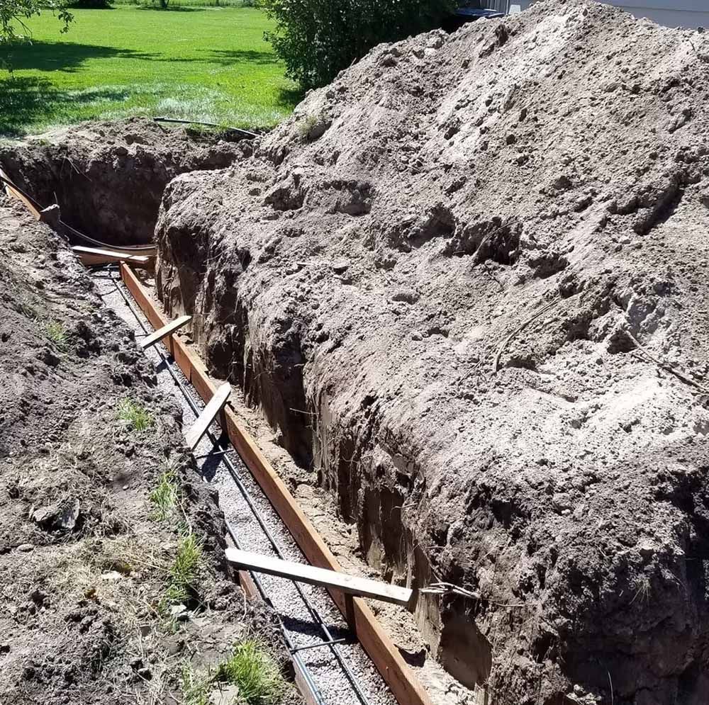 Fresh trench with large dirt piles and exposed pipe in a grassy yard