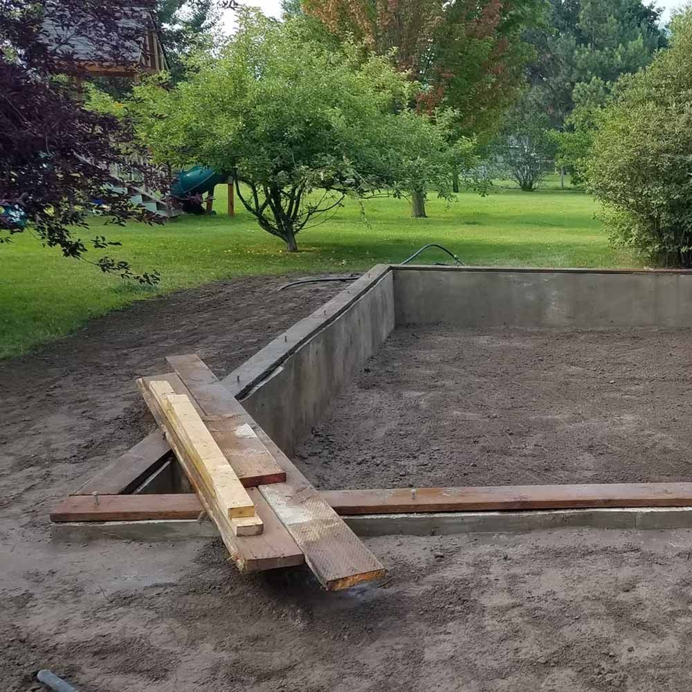 Concrete pit in a grassy yard with wooden planks forming a rough ramp or bridge.