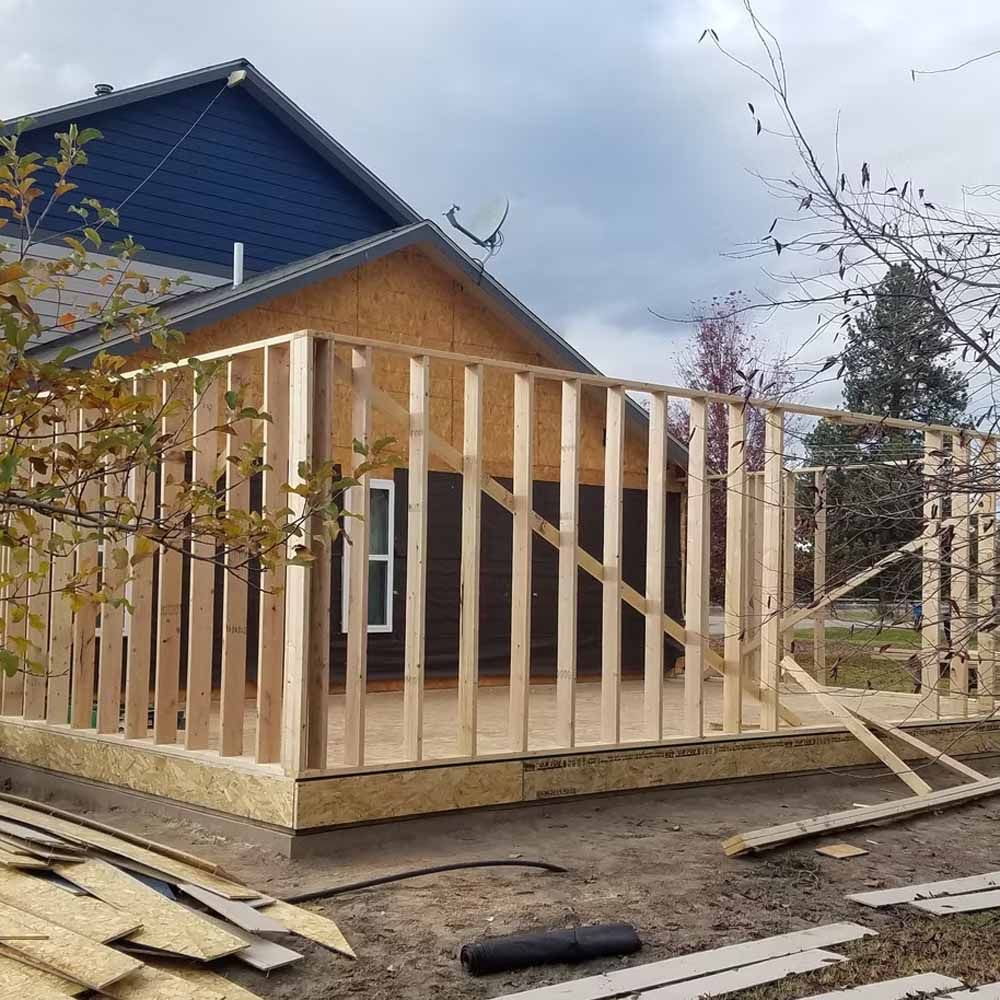 Unfinished wooden deck frame beside a house, with vertical rail posts and construction materials on the ground