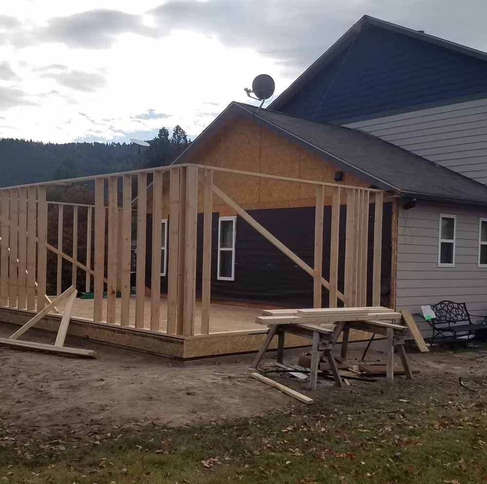 House under construction with exposed wooden framing beside a gray home and roofline.