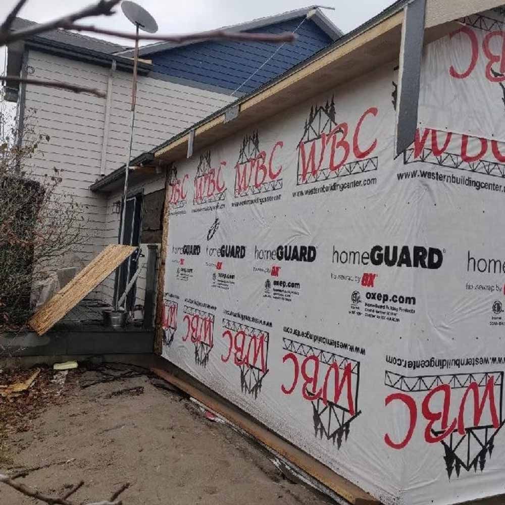 House under construction with wrapped exterior walls, metal staircase, and roof overhang in a narrow alley