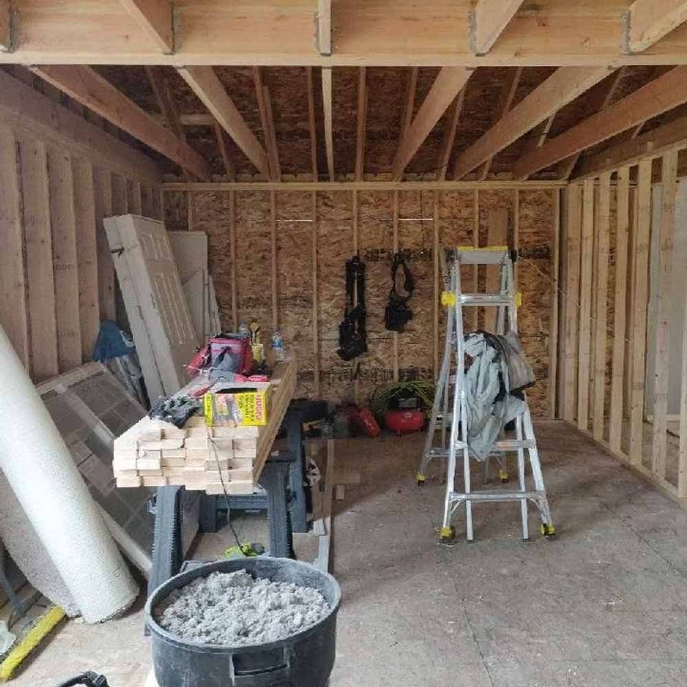 Unfinished room under construction with exposed framing, ladder, tools, and building materials on the floor.