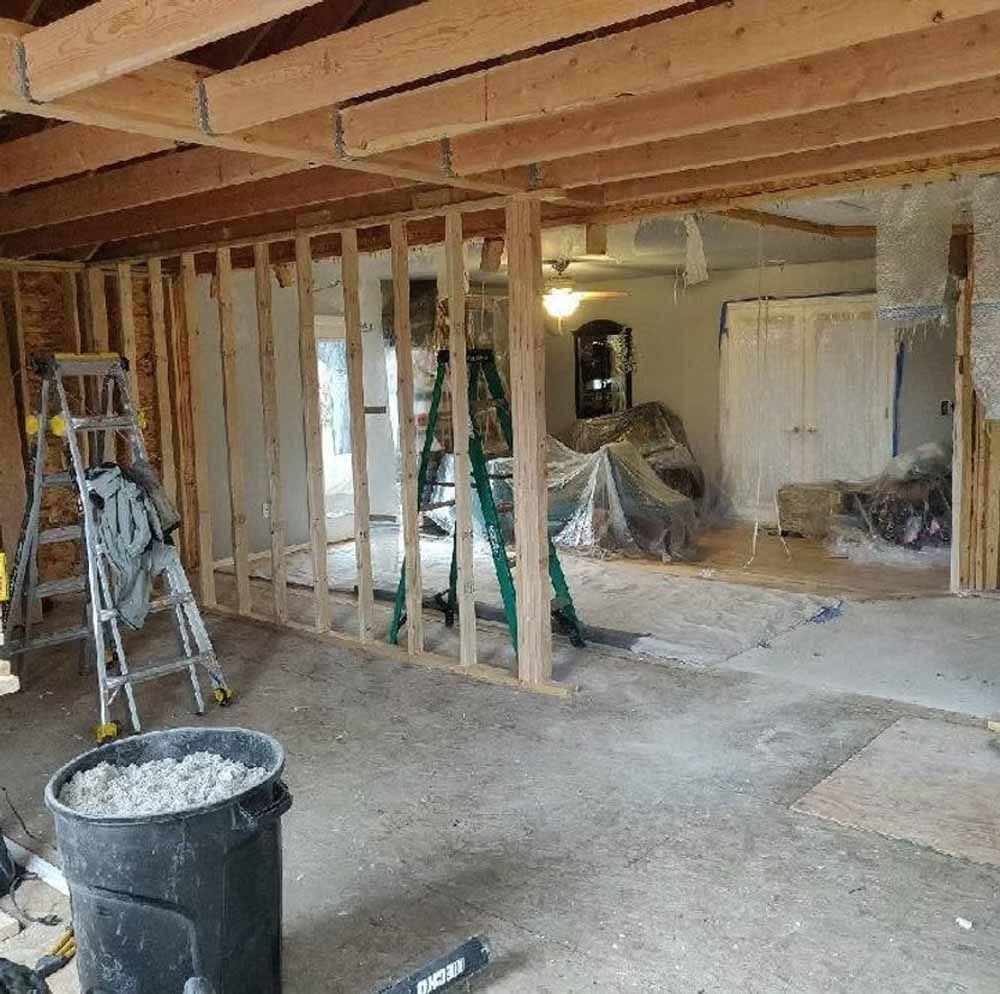 Home renovation with exposed wall studs, ladders, and construction debris in a room under remodel.