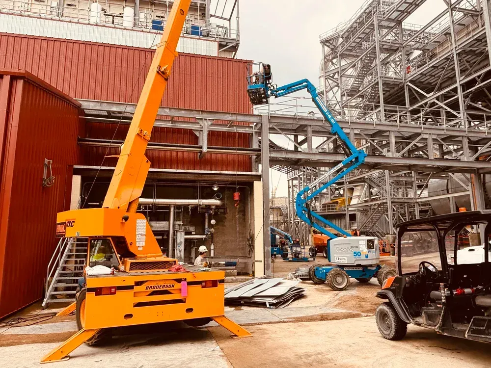 Construction site with two elevated work platforms in use. An orange platform is in the foreground, and a blue one is in the background.