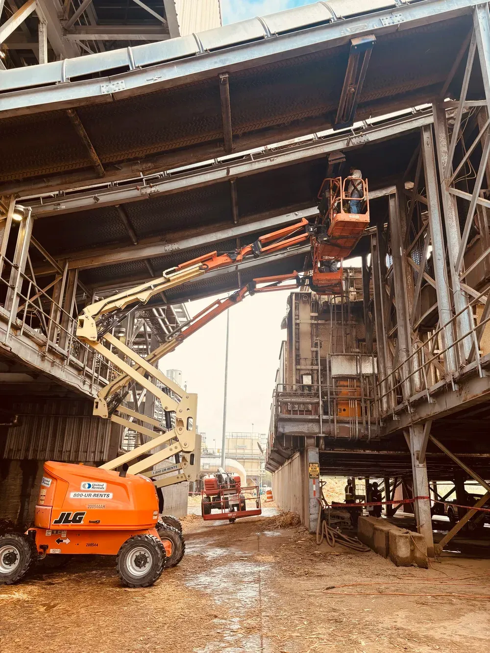 Orange lifts and construction workers repairing a large industrial structure.