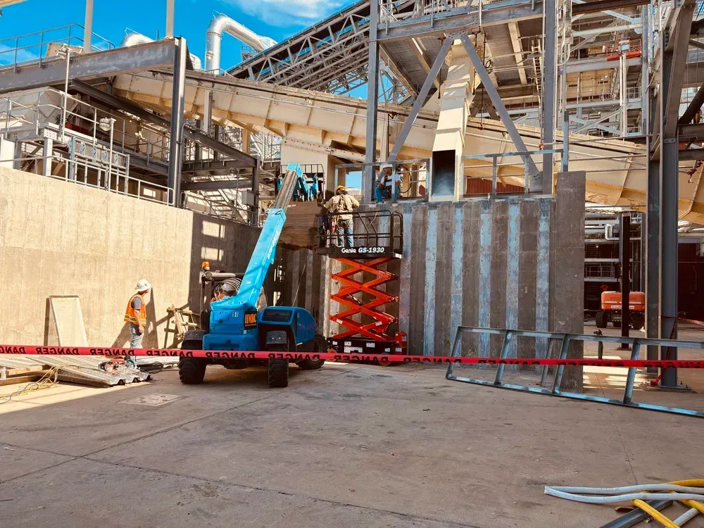 Construction site with a blue lift and orange scissor lift, workers, and red caution tape.