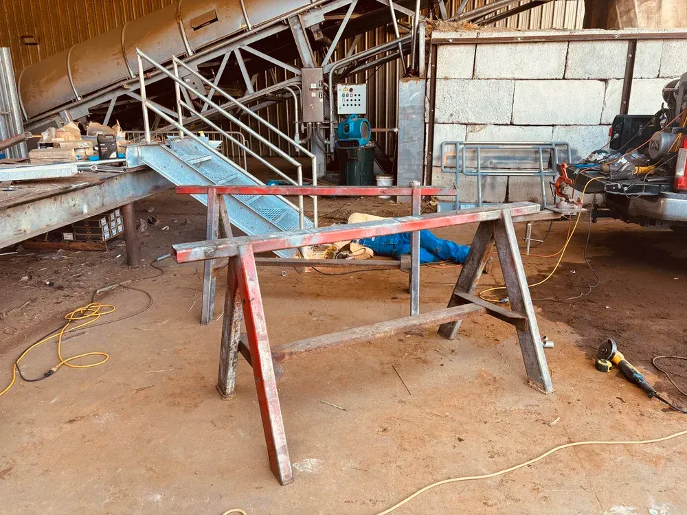 Sawhorses with metal frame in a workshop; conveyor belt in the background.