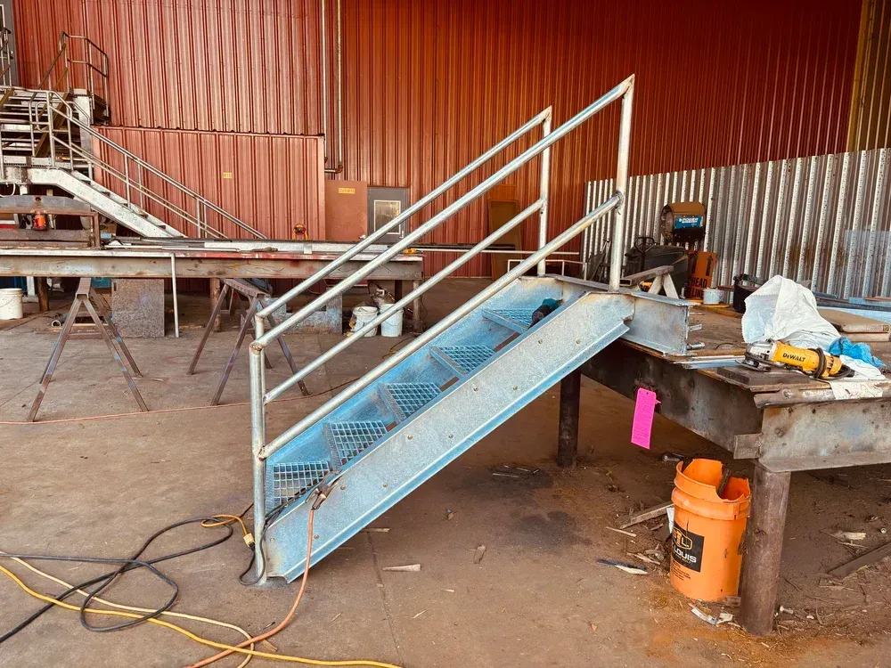 Metal stairs with handrails in an industrial setting. Orange container on the floor.