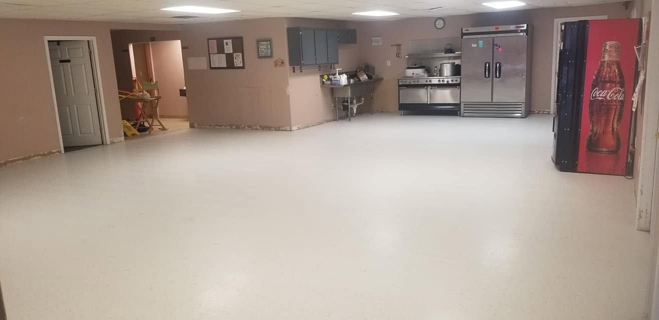 Empty beige community room with a tiled floor, tables, chairs, and a red vending machine near the back wall