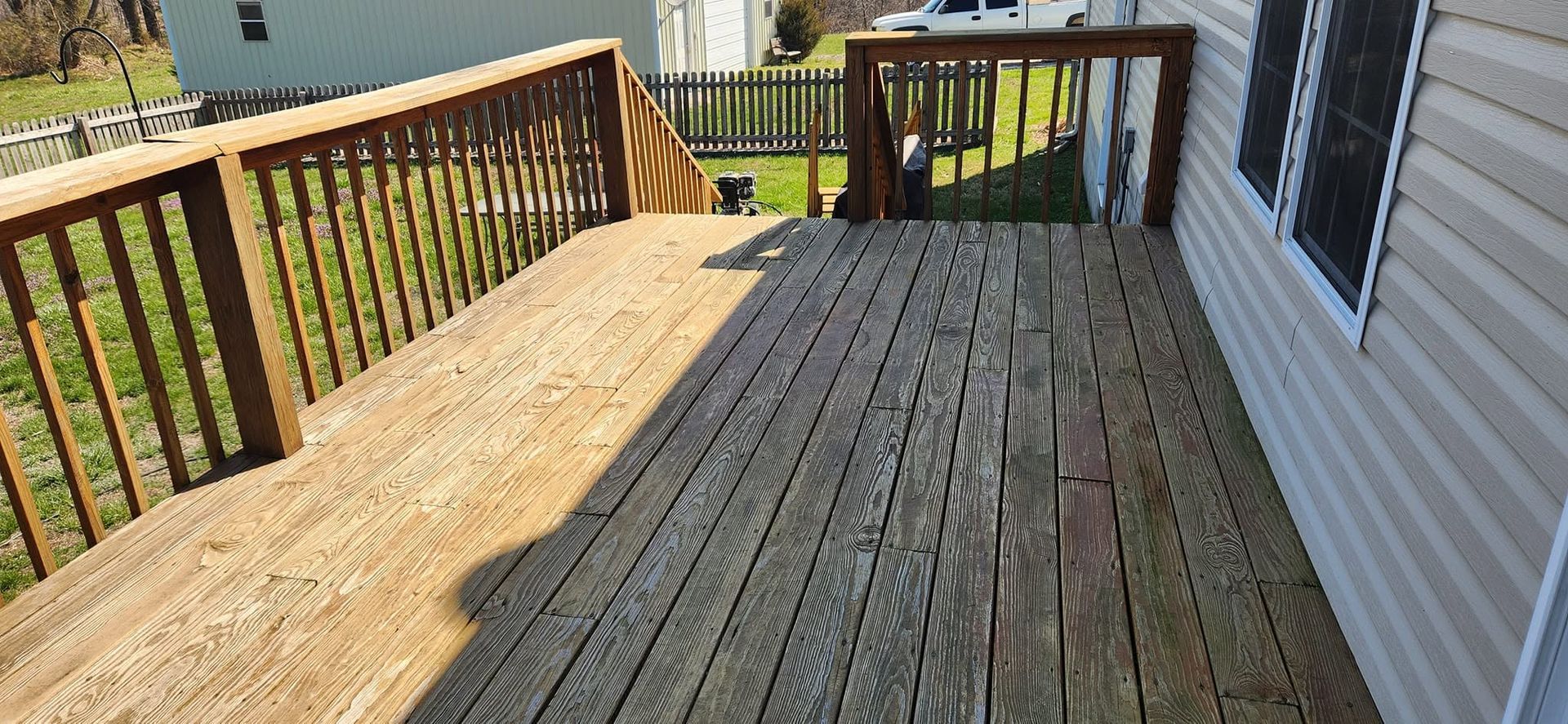 Wooden back deck with weathered boards and railing beside a house, overlooking a yard and neighboring homes