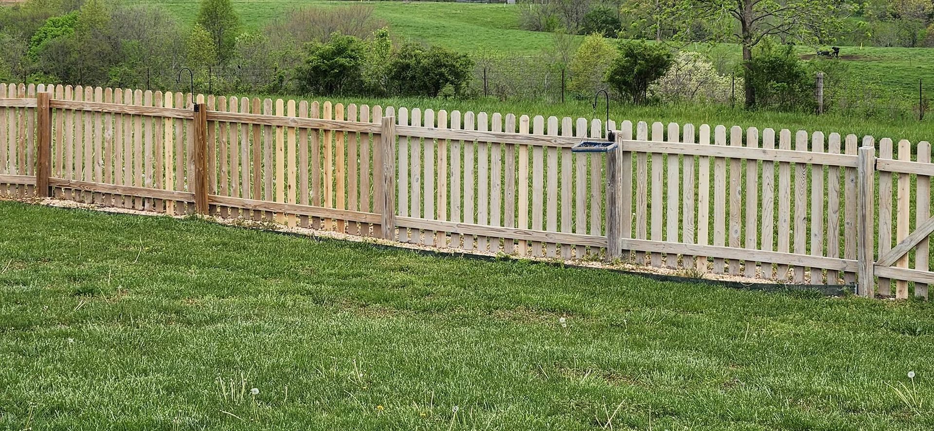 Wooden fence along a grassy field with green hills in the background