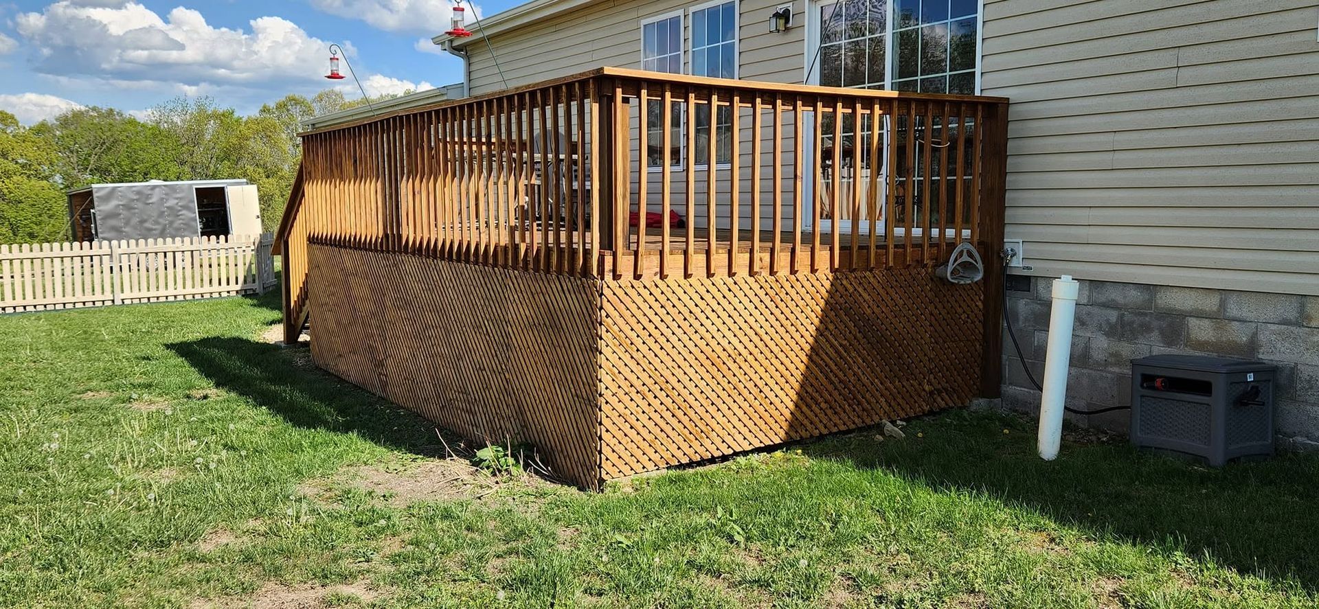Wooden backyard deck with railings beside a house, overlooking a grassy yard