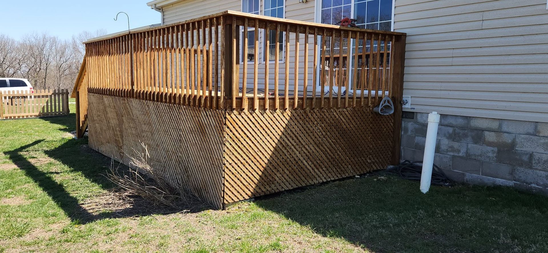 Wooden deck with lattice skirting beside a white house on a grassy yard