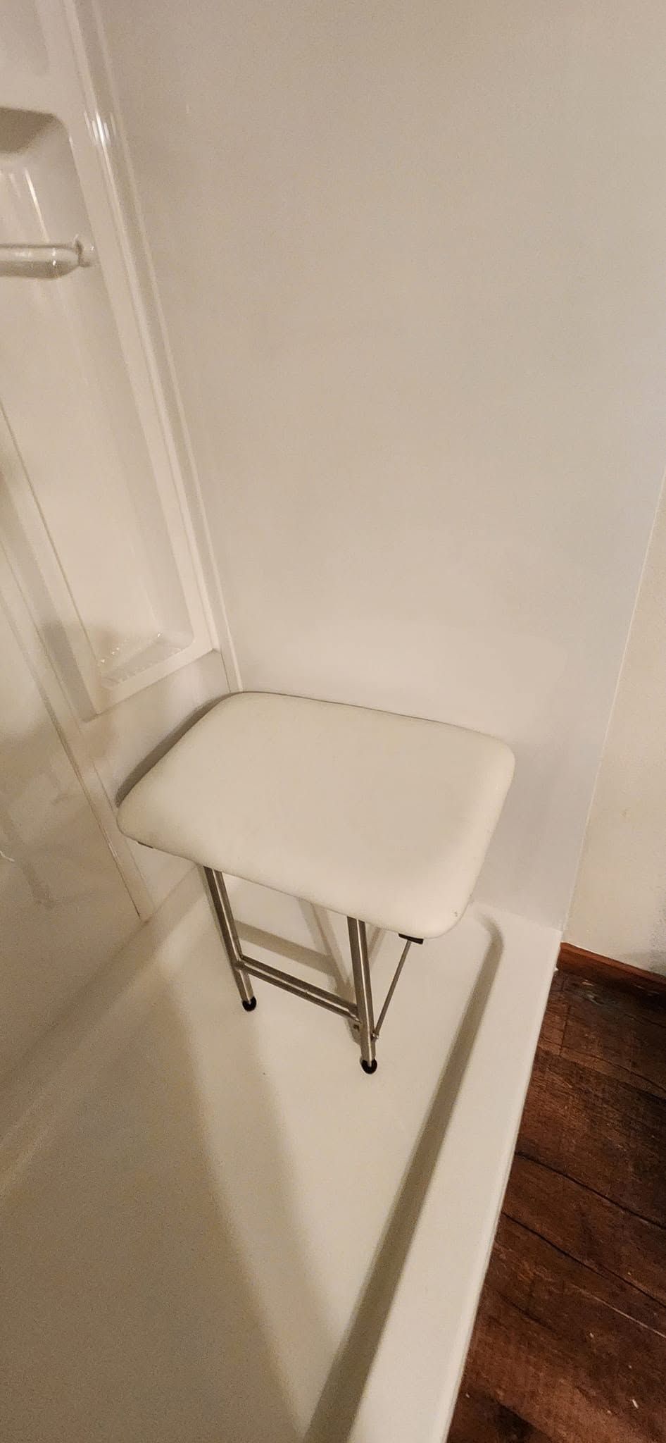 White fold-down shower seat mounted on a tiled bathroom wall