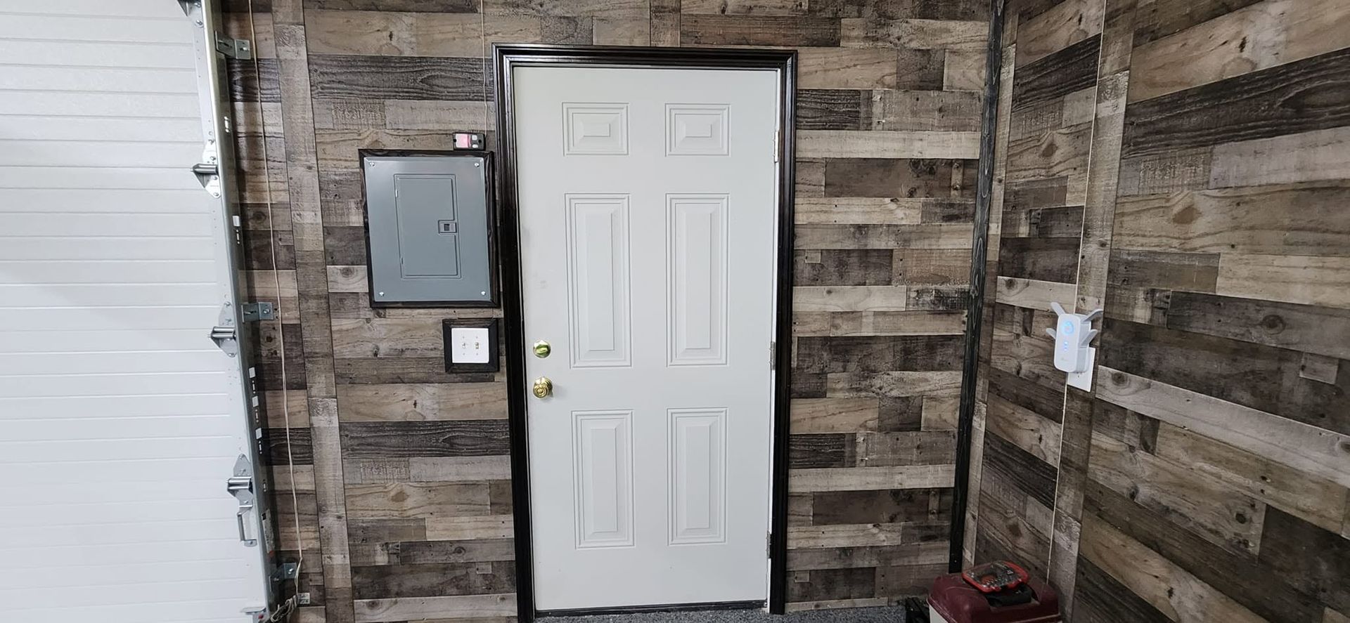 Front door in a rustic interior wall, with a gray utility box and keypad to the left.