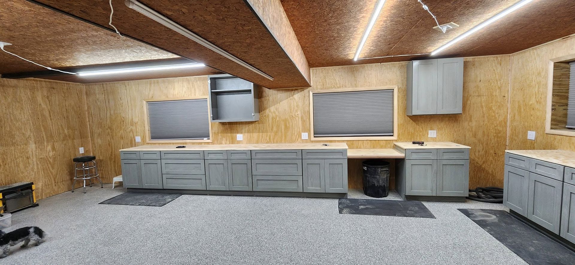 Basement workshop with gray cabinets, wood-paneled walls, and a speckled floor under slanted ceiling lights