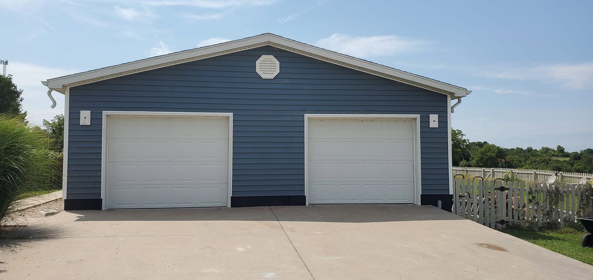 Blue two-car garage with white doors on a concrete driveway under a clear sky