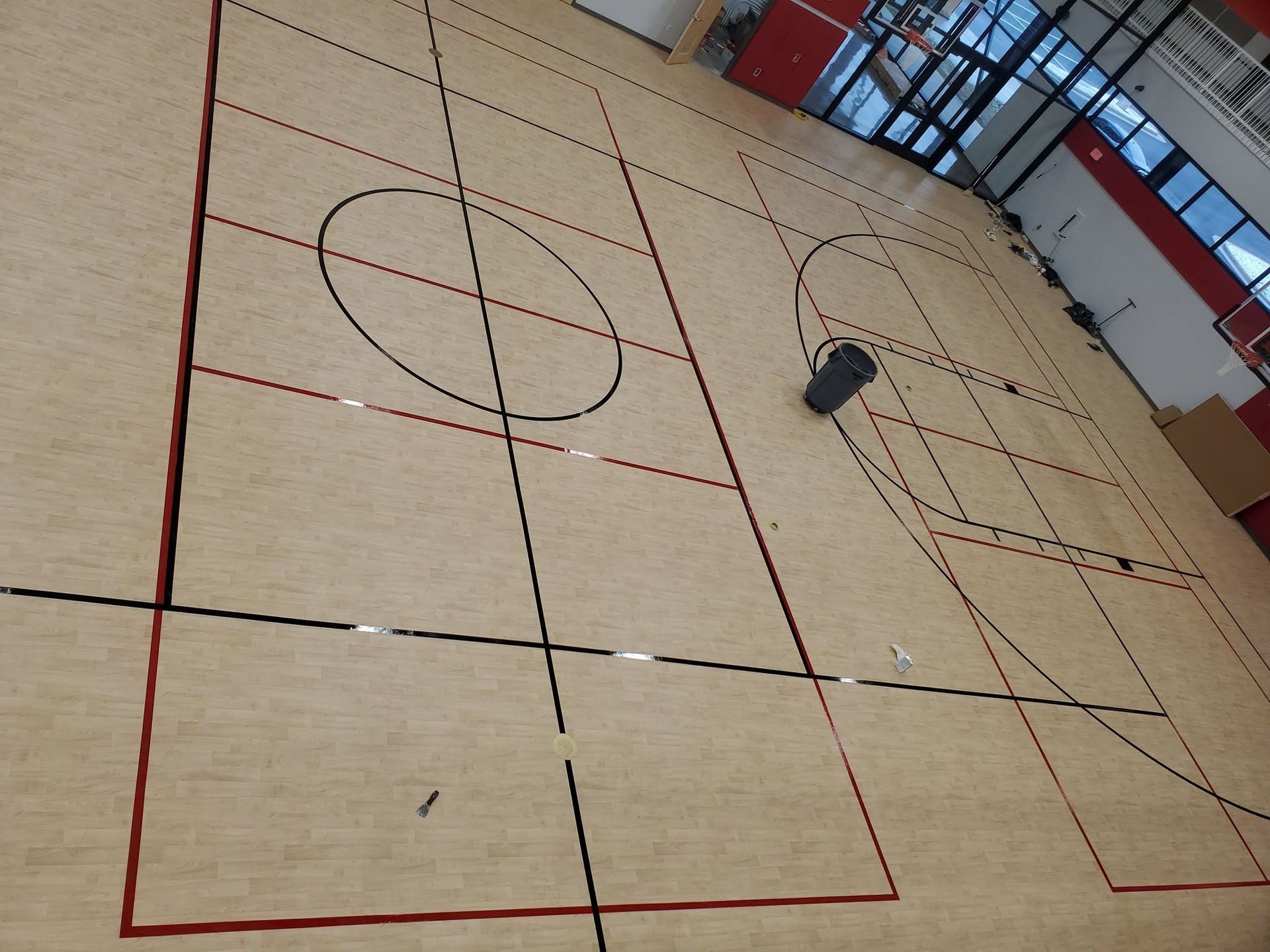 Indoor gym floor with red court lines and a central circle, viewed at an angle.