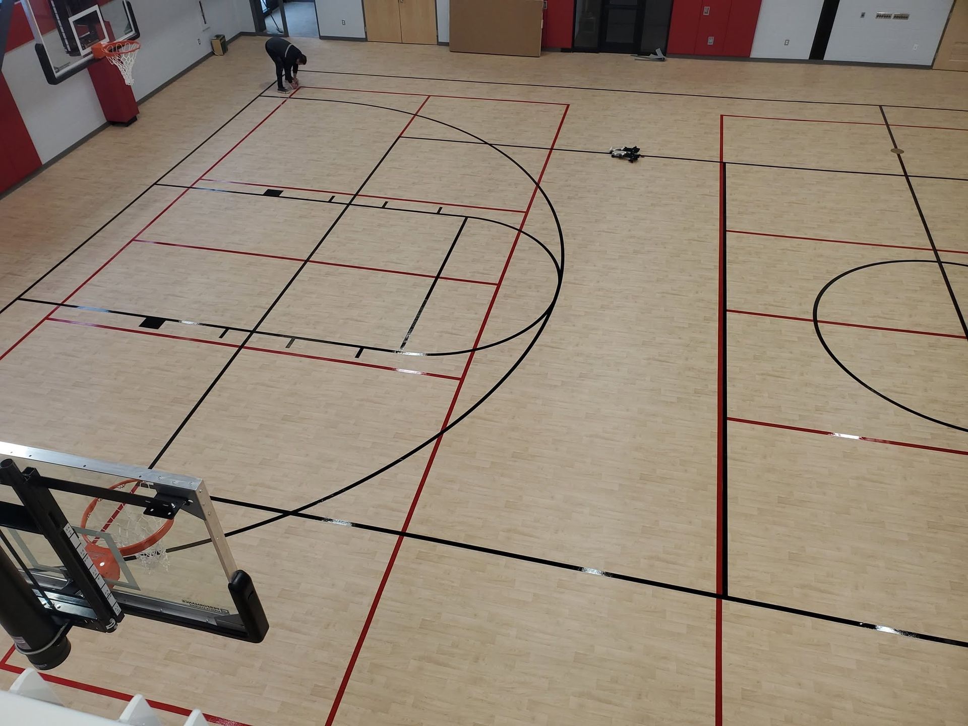 Indoor gym floor with basketball court lines and a person in the distance near the wall
