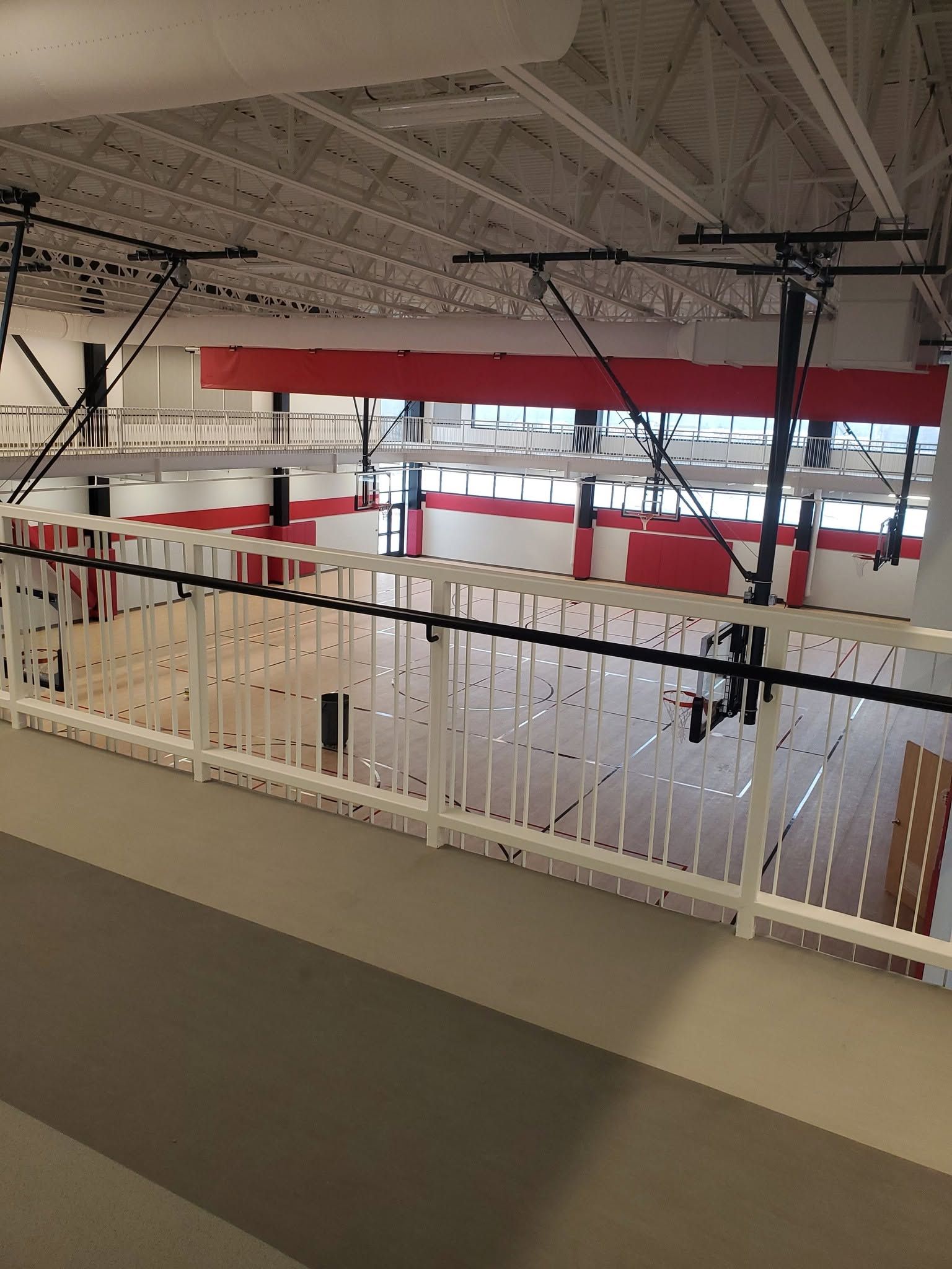 Mezzanine overlooking an indoor space with white railing, red beams, and exposed ceiling pipes