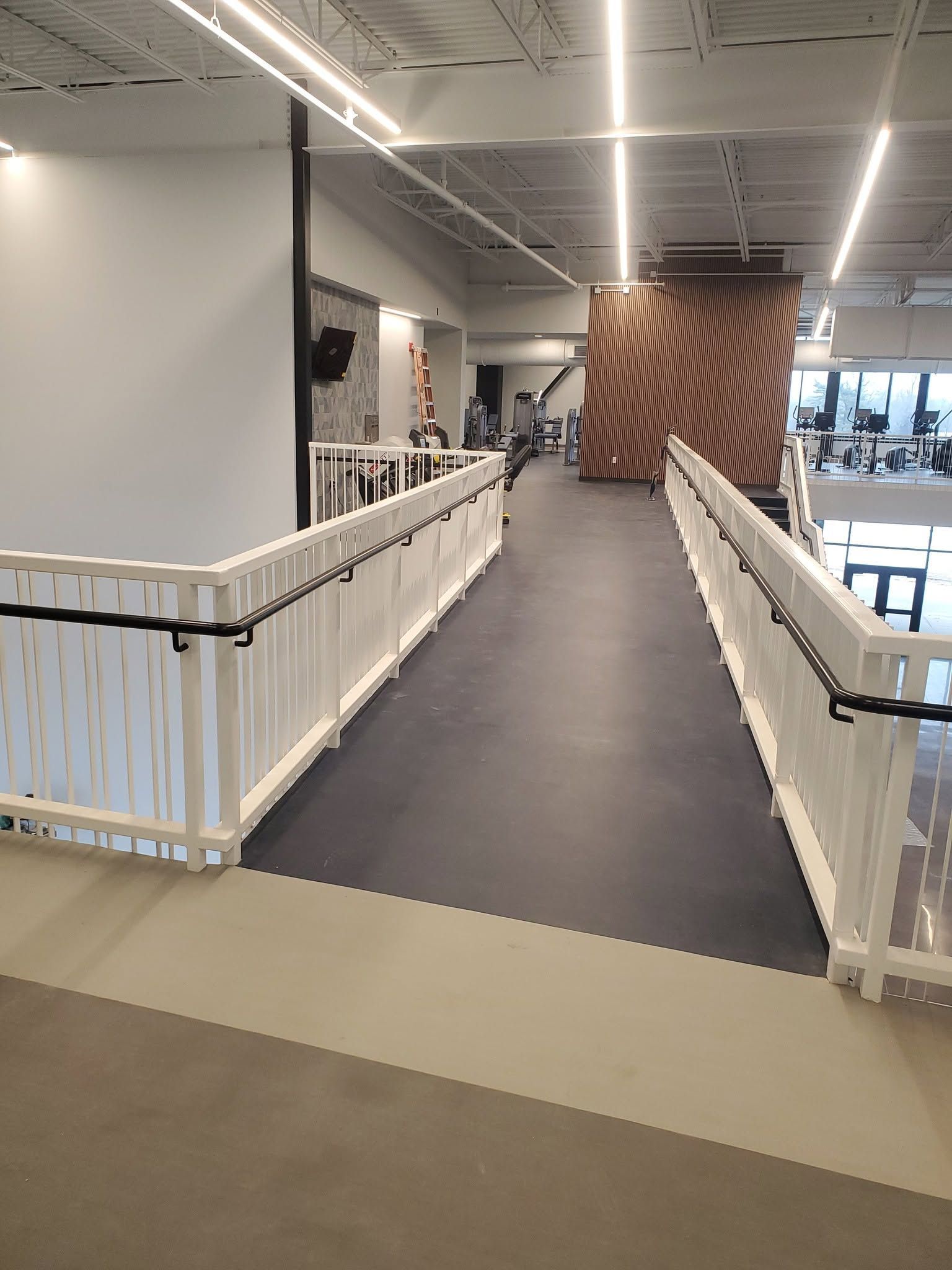 Indoor ramp with white railings and gray carpet leading into a modern office or lobby area.