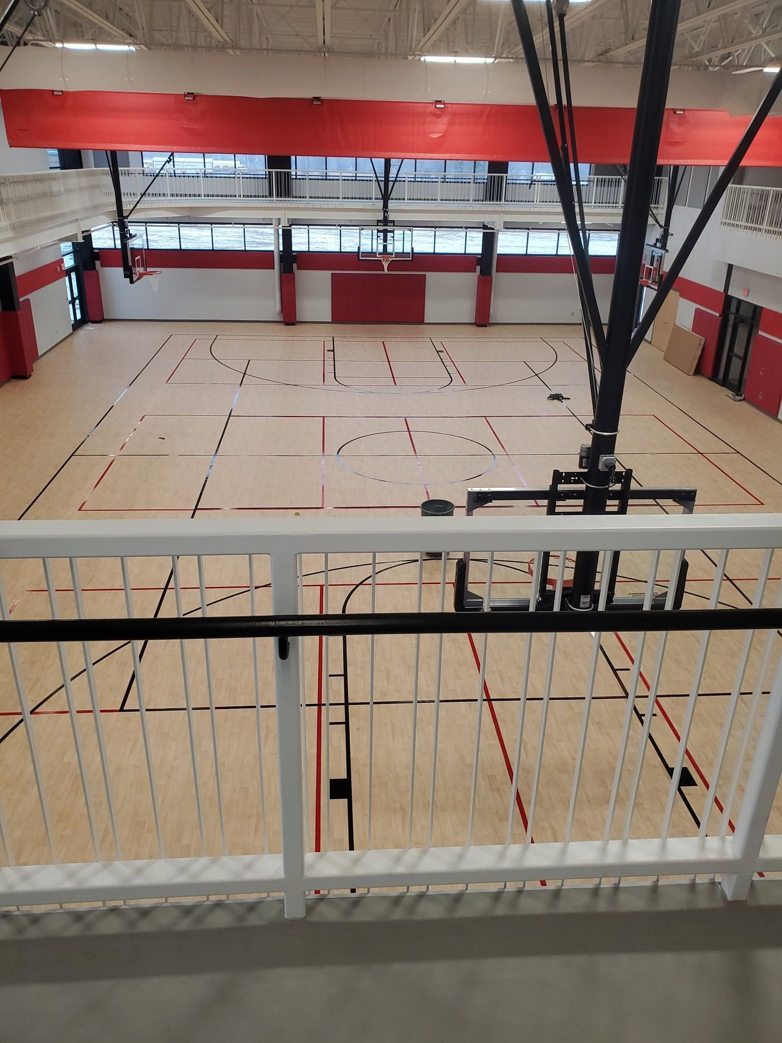 Empty indoor basketball court with red and white bleachers viewed from an elevated balcony