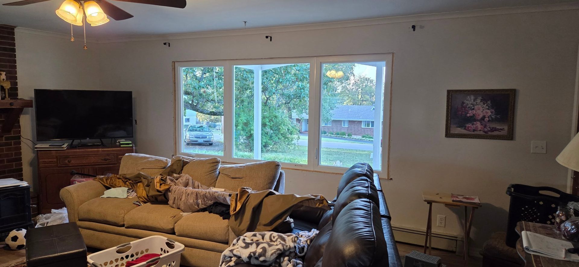 Living room with beige sofa, large window, TV, fireplace, and ceiling fan