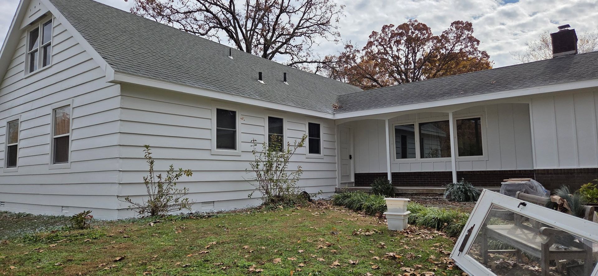 White house with a screened porch and leaf-covered yard in autumn