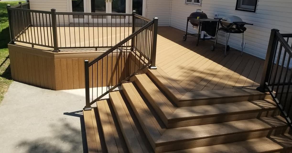 Wooden deck stairs leading to a raised patio beside a house, with railings and outdoor furniture.