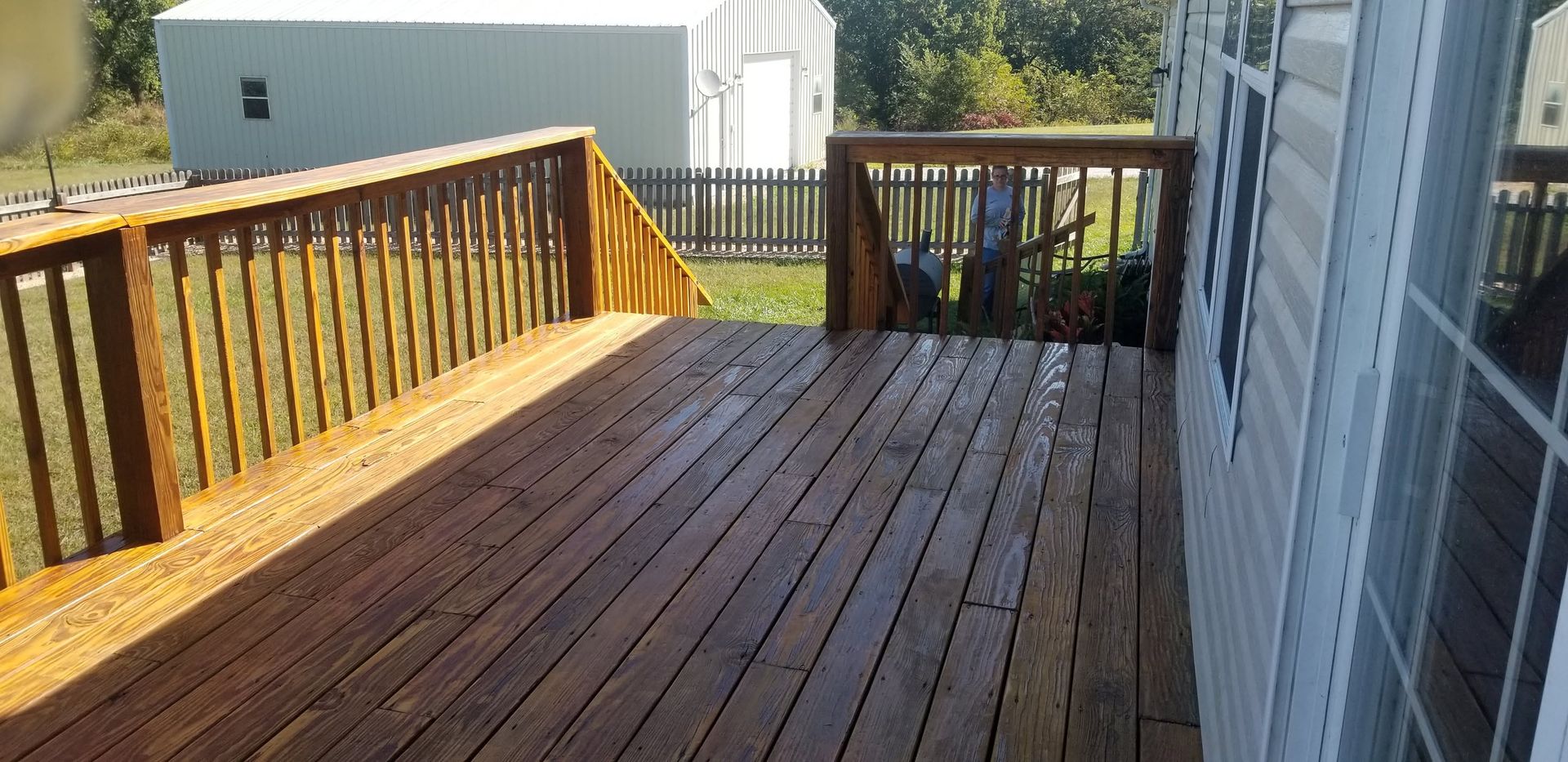 Wooden deck with black railing beside a house, lit by sunlight.
