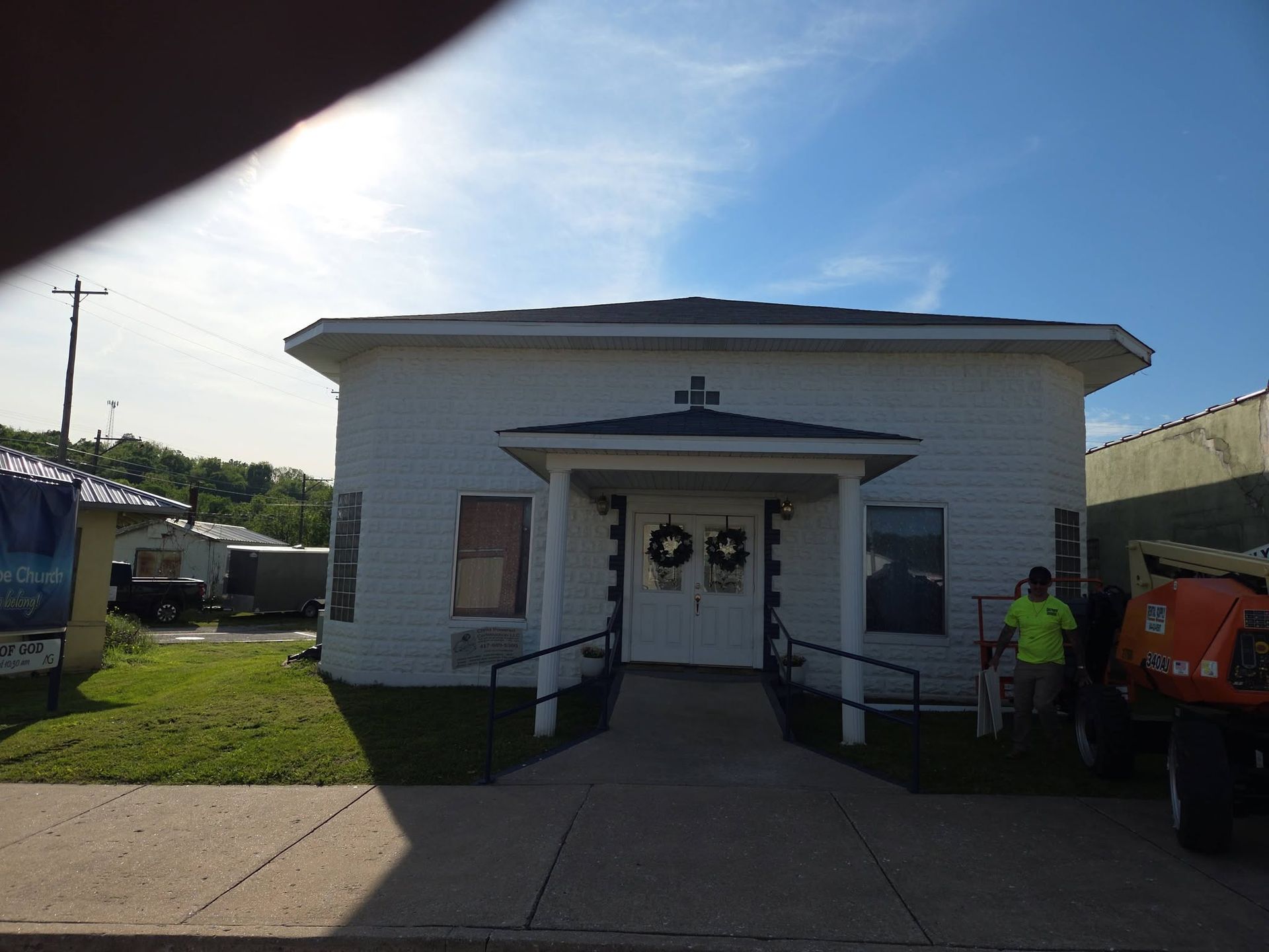 Small white building with wreath-decorated doors, ramp, and a person standing beside an orange truck.