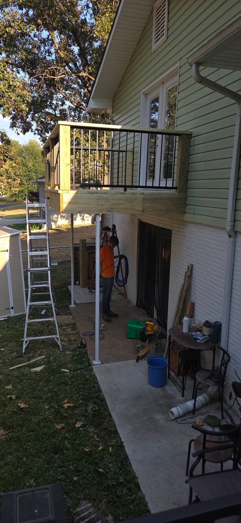 Backyard side of a house with a second-floor balcony, ladder, and patio items below