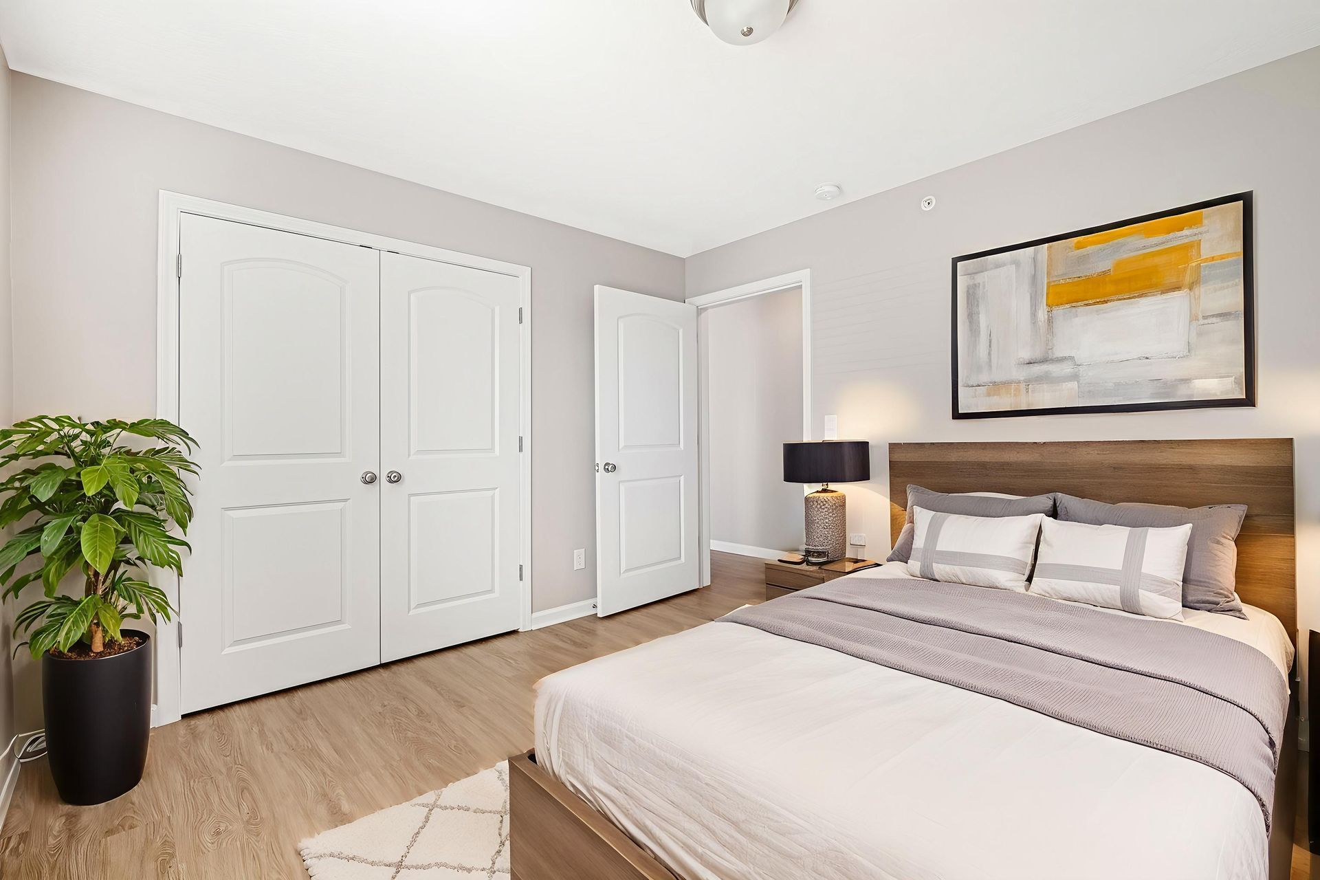 Bright bedroom with a bed, nightstand, closet doors, and wall art in a neutral-toned room