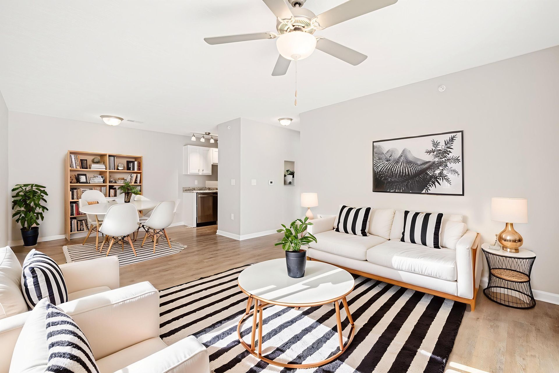 Bright living room with striped rug, white sofa, coffee table, ceiling fan, and dining area in the background