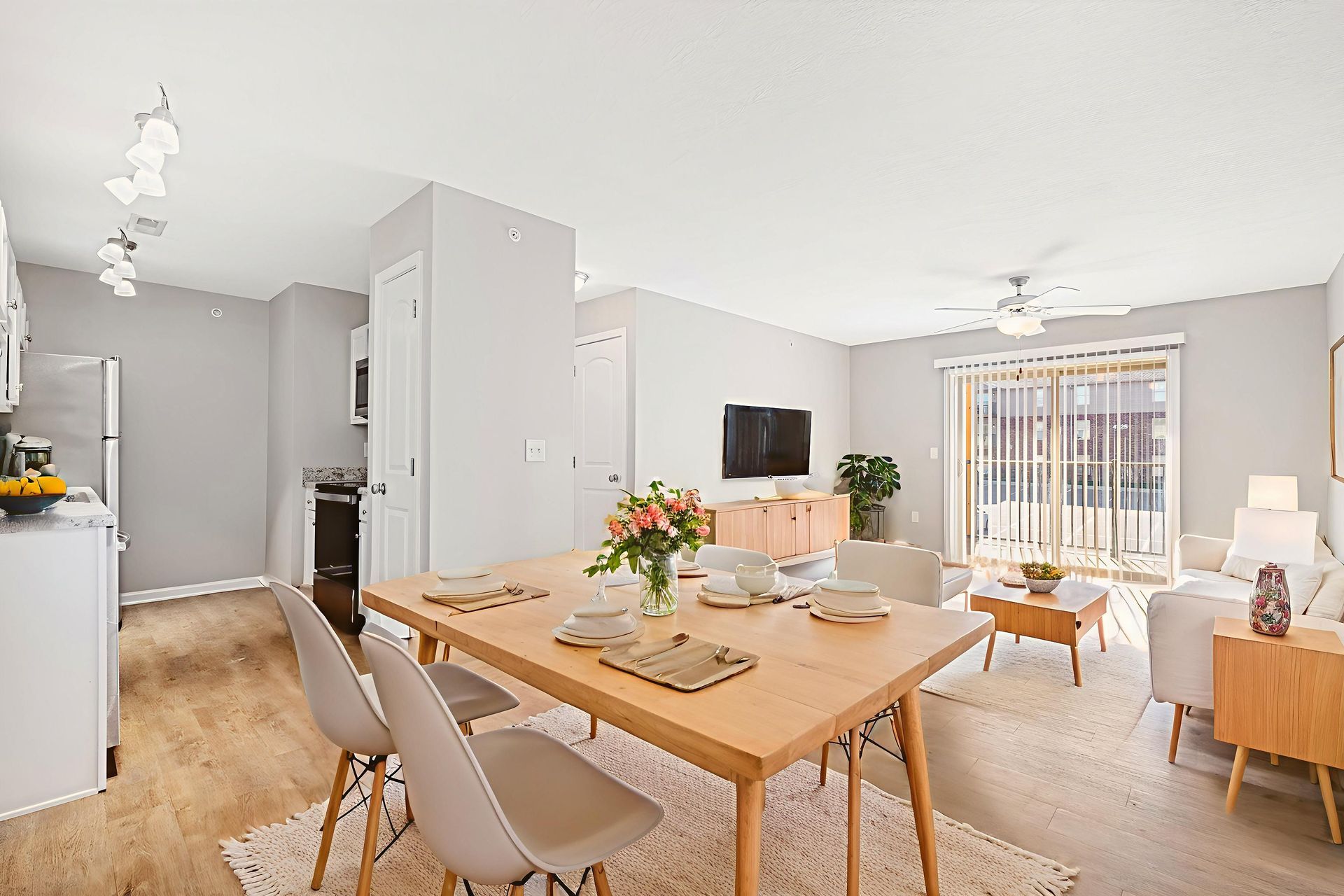 Bright open dining and living room with wood table, beige chairs, wall TV, and sliding glass doors