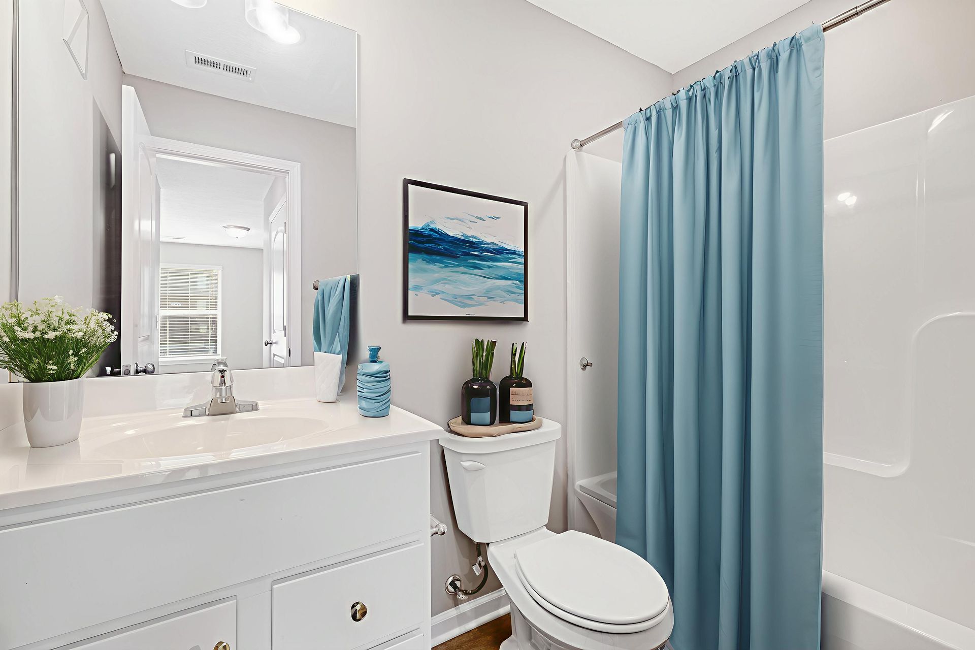 Bright bathroom with white vanity, toilet, and shower curtain in blue.