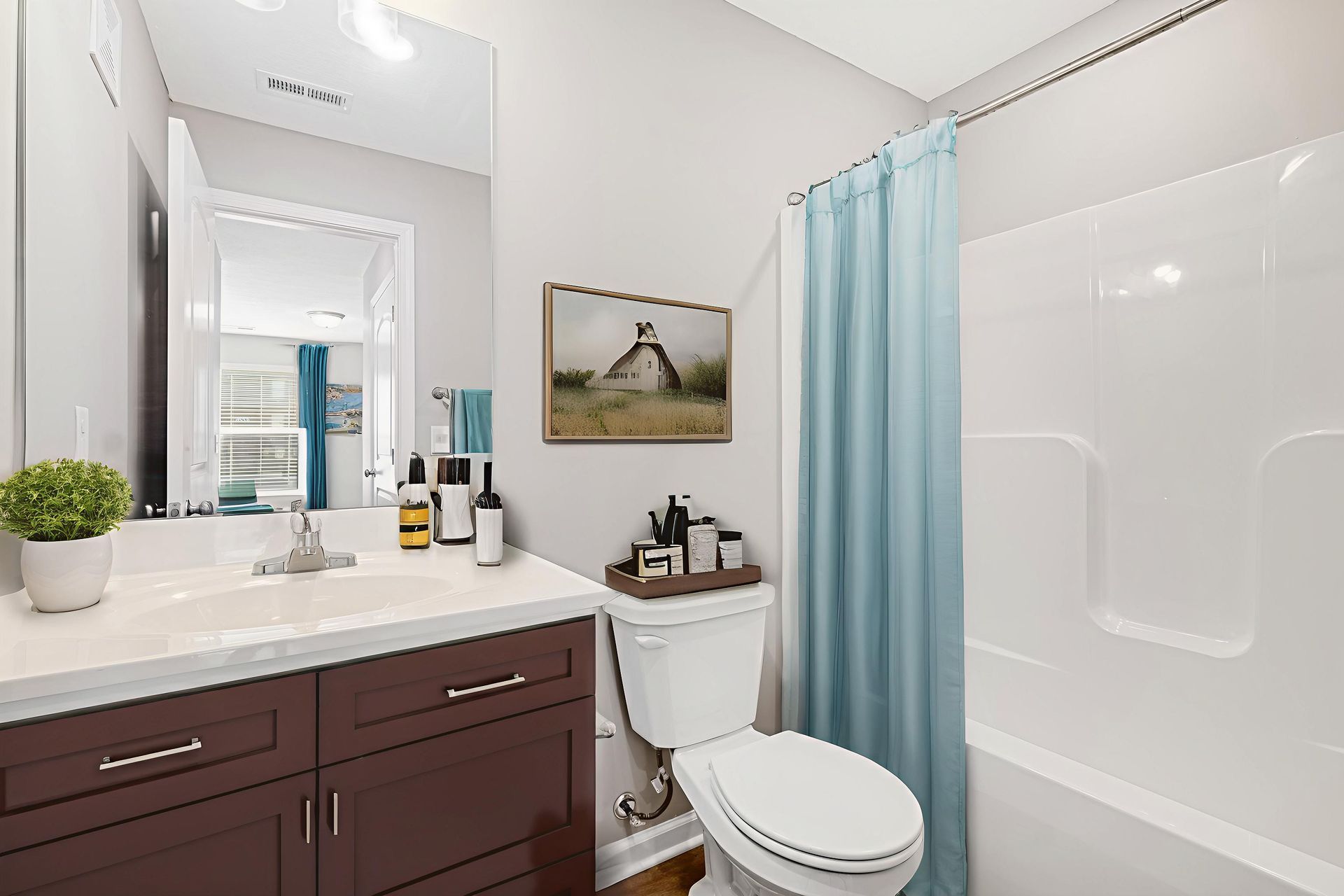 Bright bathroom with dark vanity, white tub, toilet, and light blue shower curtain.