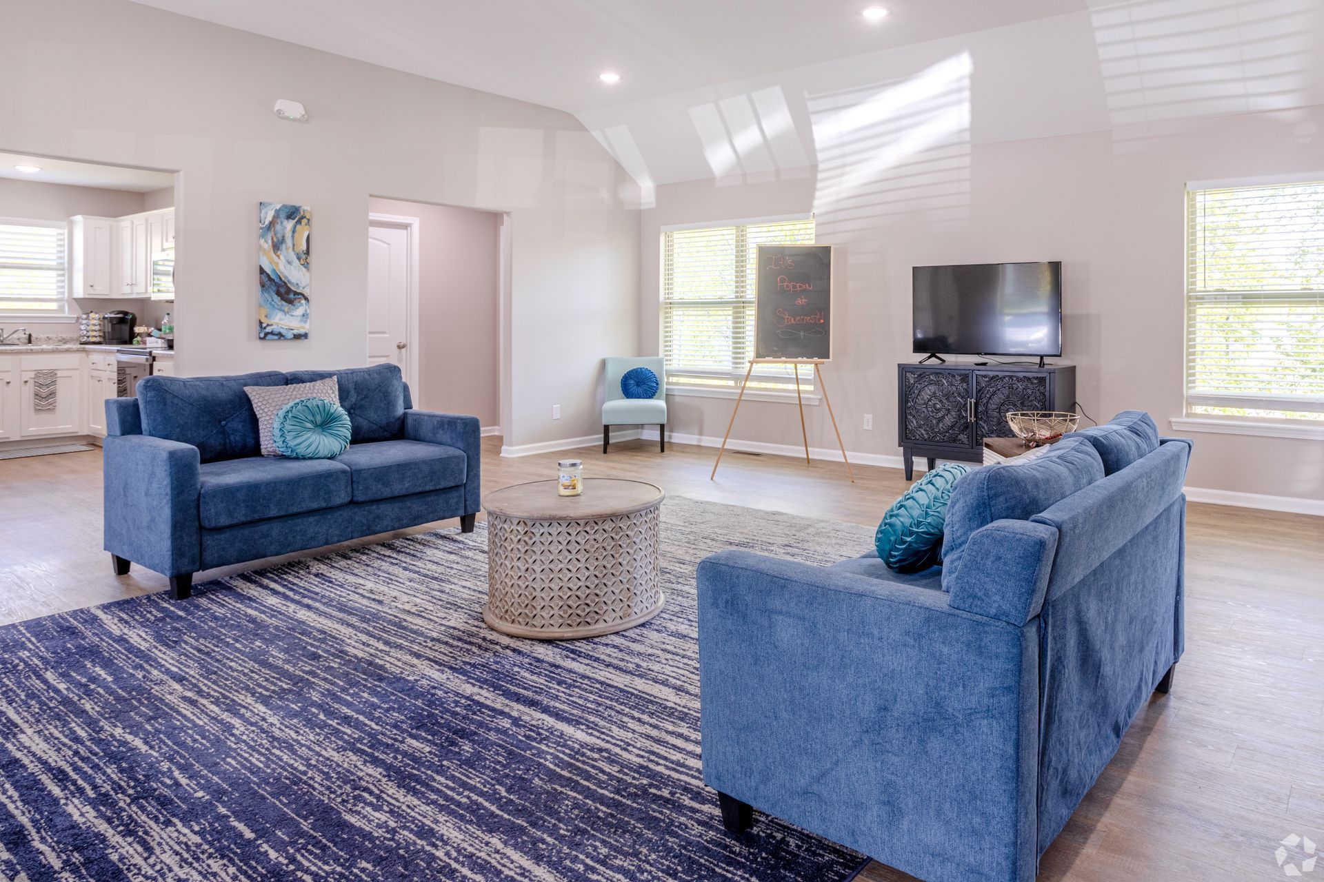 Bright living room with blue sofas, patterned rug, wicker table, and sunlight streaming through windows