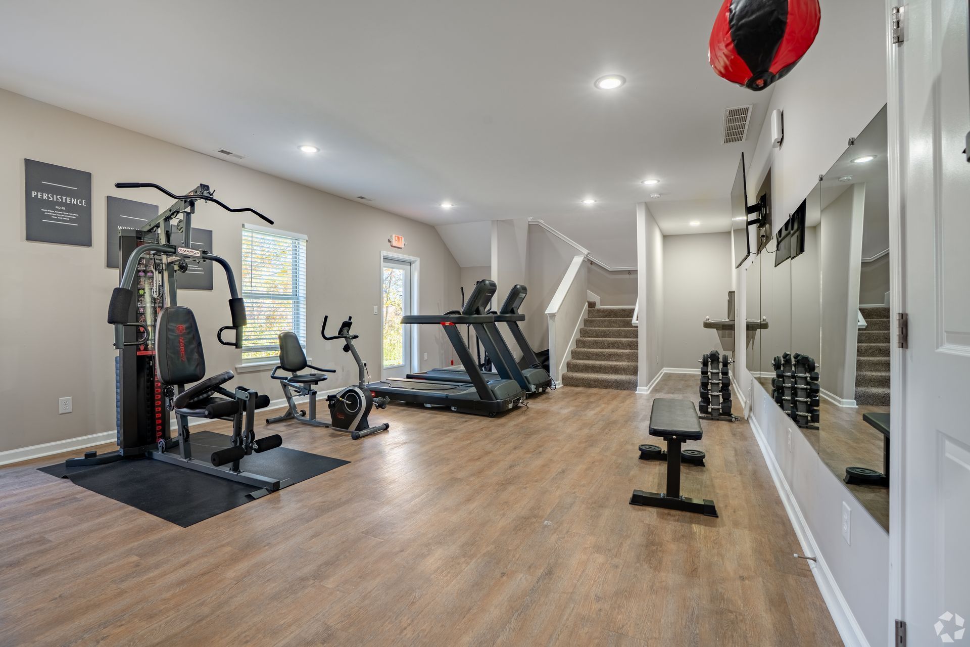 Home gym with exercise machines, wood floors, wall mirror, and stairs in the background