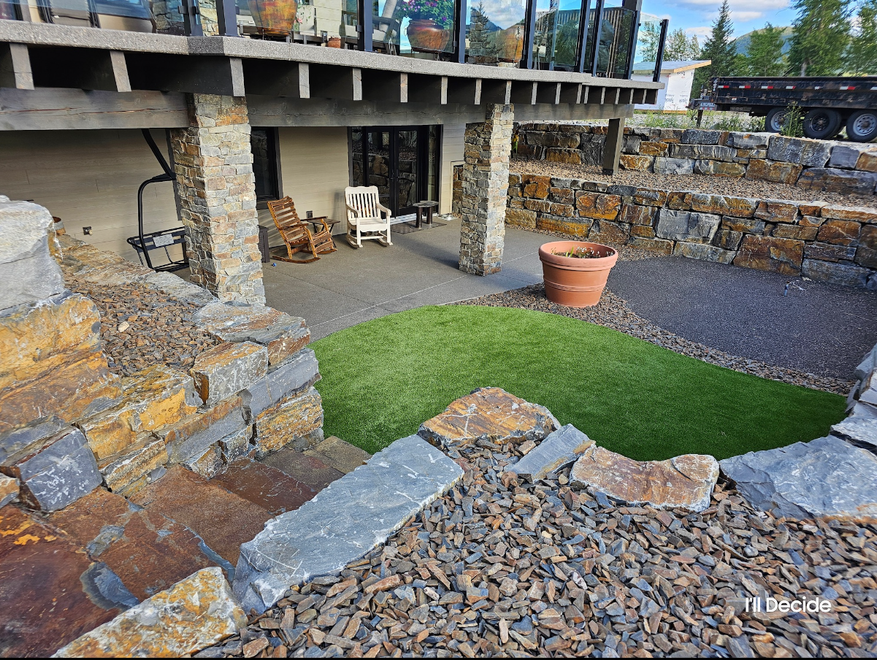 Stone patio with a small green lawn, gravel, and a covered seating area supported by stone pillars.