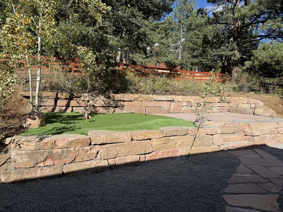 Stone terraced garden with green lawn, trees, and a paved path in sunlight