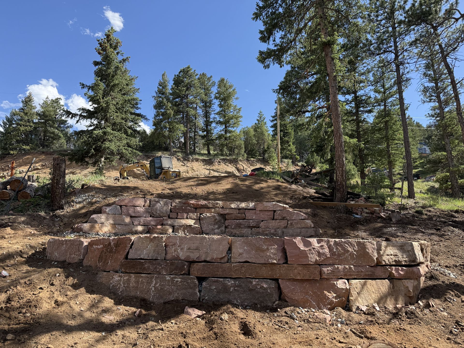 Stone steps on a forested hillside under a blue sky, with tall pine trees surrounding the scene