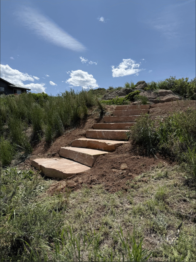 Stone steps on a grassy dirt hillside under a bright blue sky with clouds