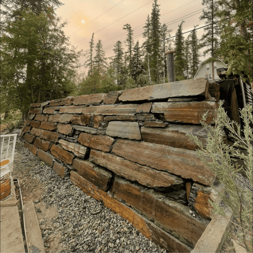 Stacked wooden wall panels beside gravel, with trees and a smoky sky in the background.