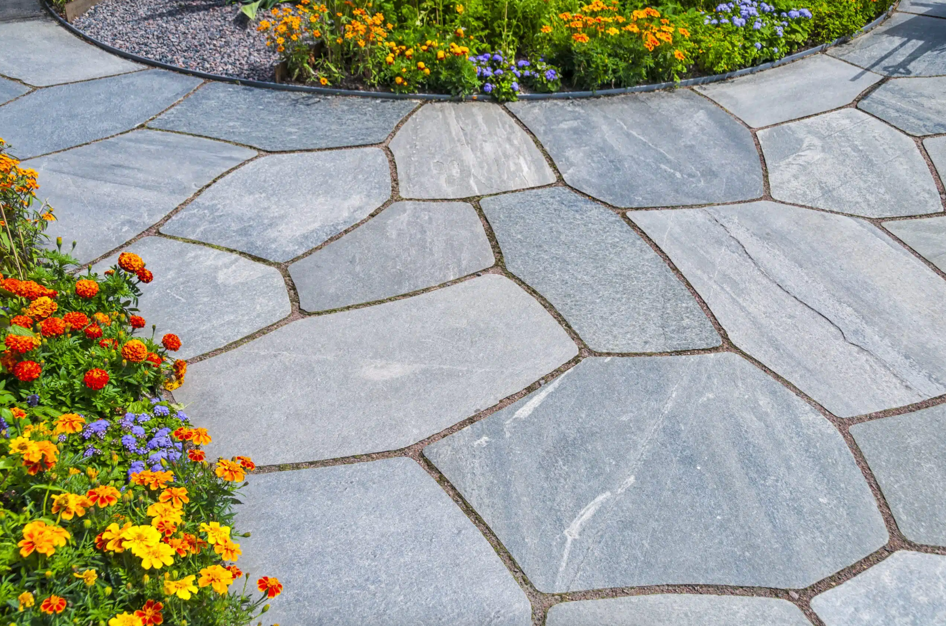 Stone garden path with irregular gray pavers bordered by colorful flowers