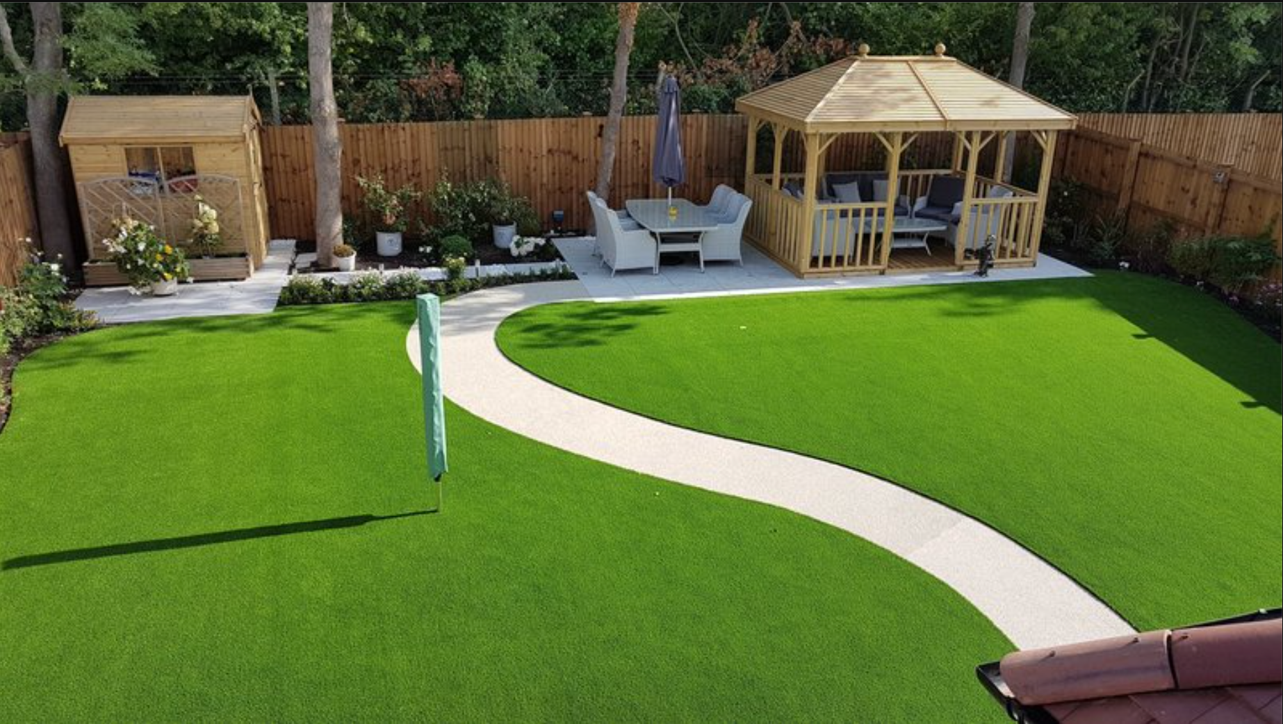 Backyard with bright green turf, a winding white path, patio seating, and a wooden gazebo