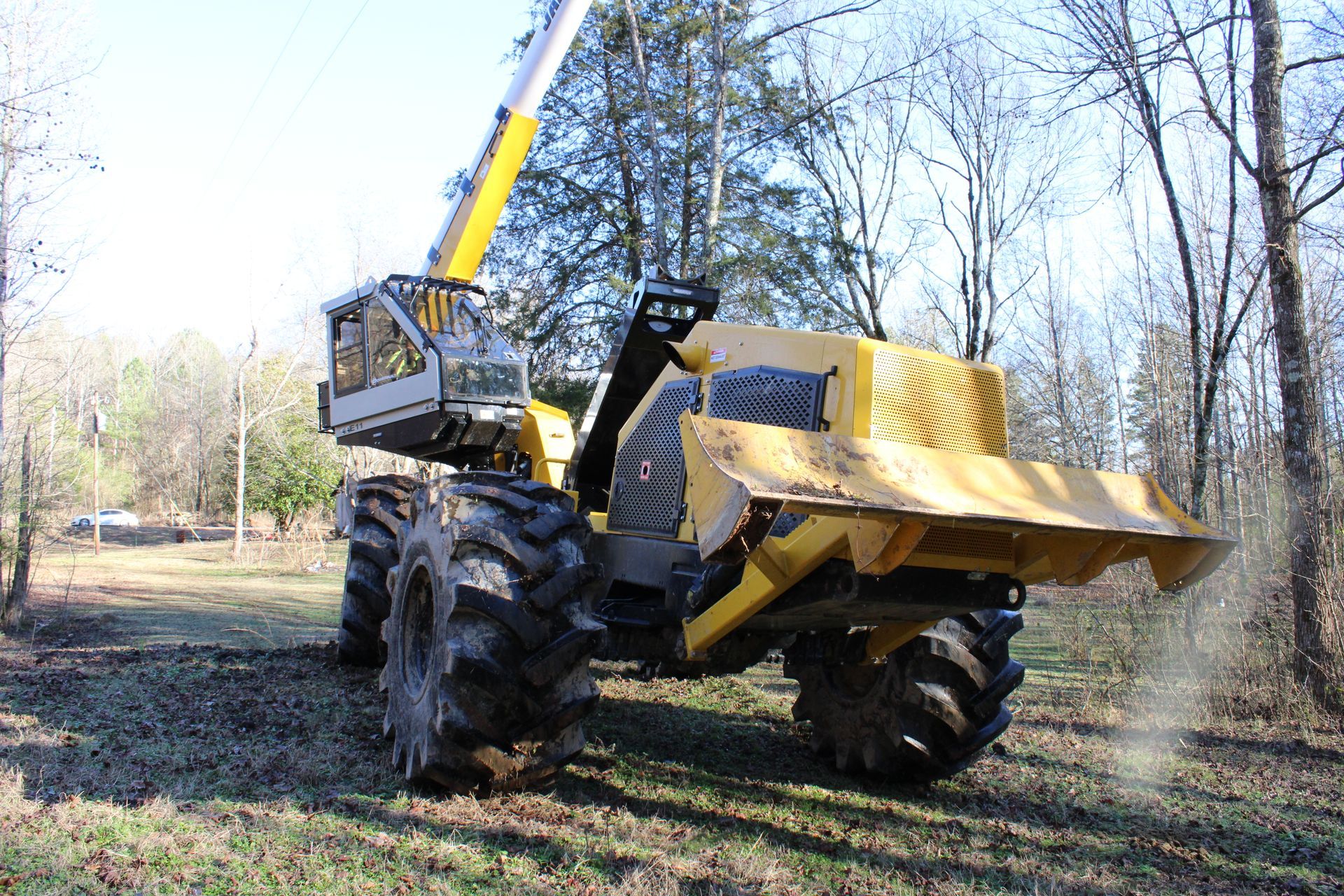 Yellow tractor with front loader lifting dirt in a wooded field
