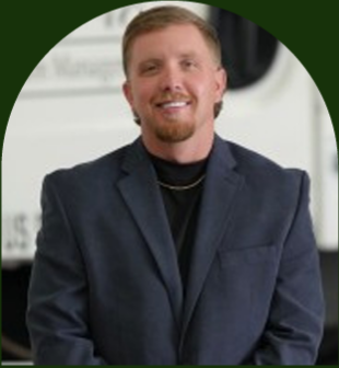 Smiling man in a dark blazer and black shirt, seated against a blurred indoor background. Smiling man in a dark blazer and black shirt, seated against a blurred indoor background.