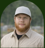 Man in a light gray cap and tan shirt, standing outdoors with a blurred green background. Man in a light gray cap and tan shirt, standing outdoors with a blurred green background.