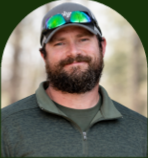 Smiling bearded man in a dark green jacket and cap, wearing reflective sunglasses outdoors Smiling bearded man in a dark green jacket and cap, wearing reflective sunglasses outdoors